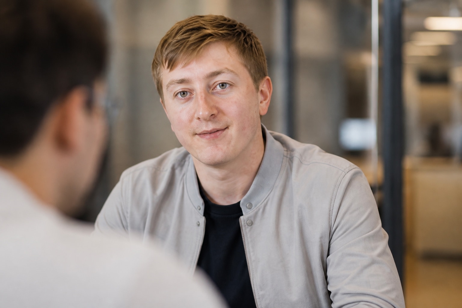 Moritz Zinecker in einer hellgrauen Jacke während eines sitzenden Gesprächs im Büro